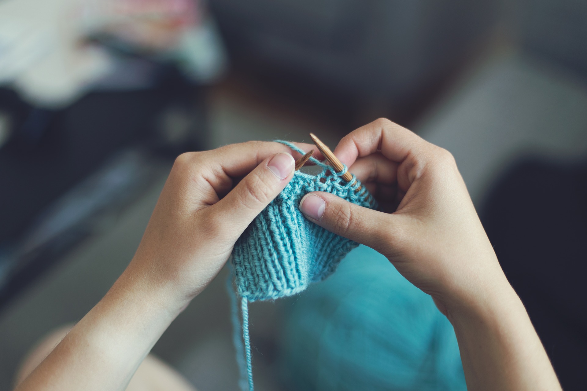 A person knitting a small square using green wool.
